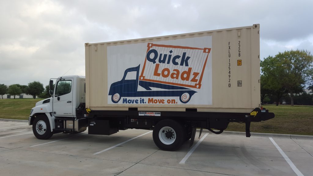 A QuickLoadz 20k Super Bed with a 20' shipping container loaded. The container has the QuickLoadz logo painted on the side.