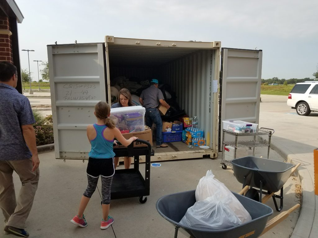 People unloading hurricane relief supplies from a shipping container on the ground.