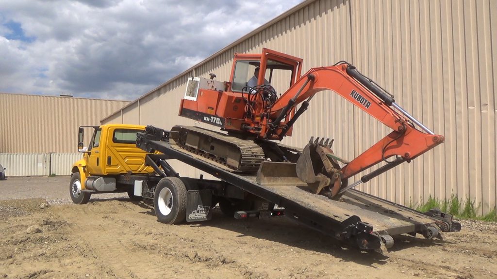 A Quickloadz 20k Super Bed with a backhoe loaded on the bed. The bed is at an angle.
