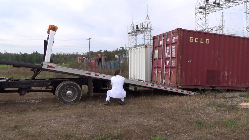 Someone squatted down next to a QuickLoadz trailer, unloading a container. 
